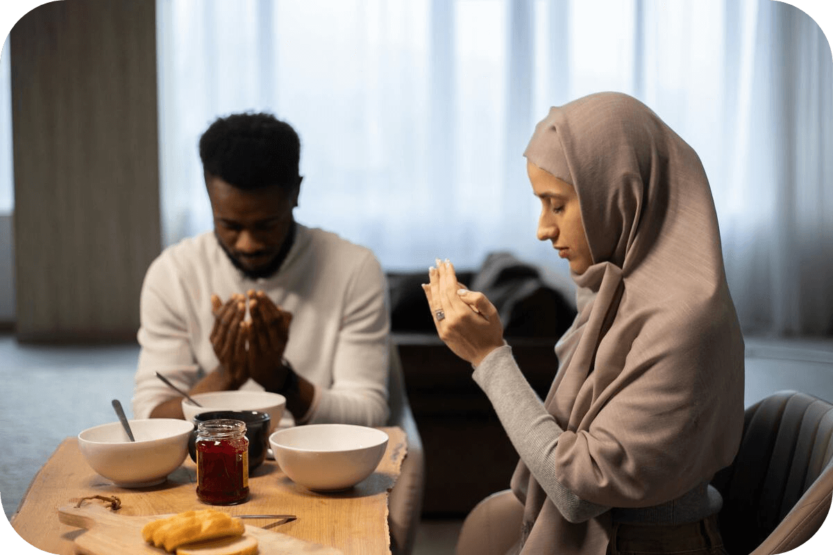 A Muslim man and woman making dua before the meal at the dining table