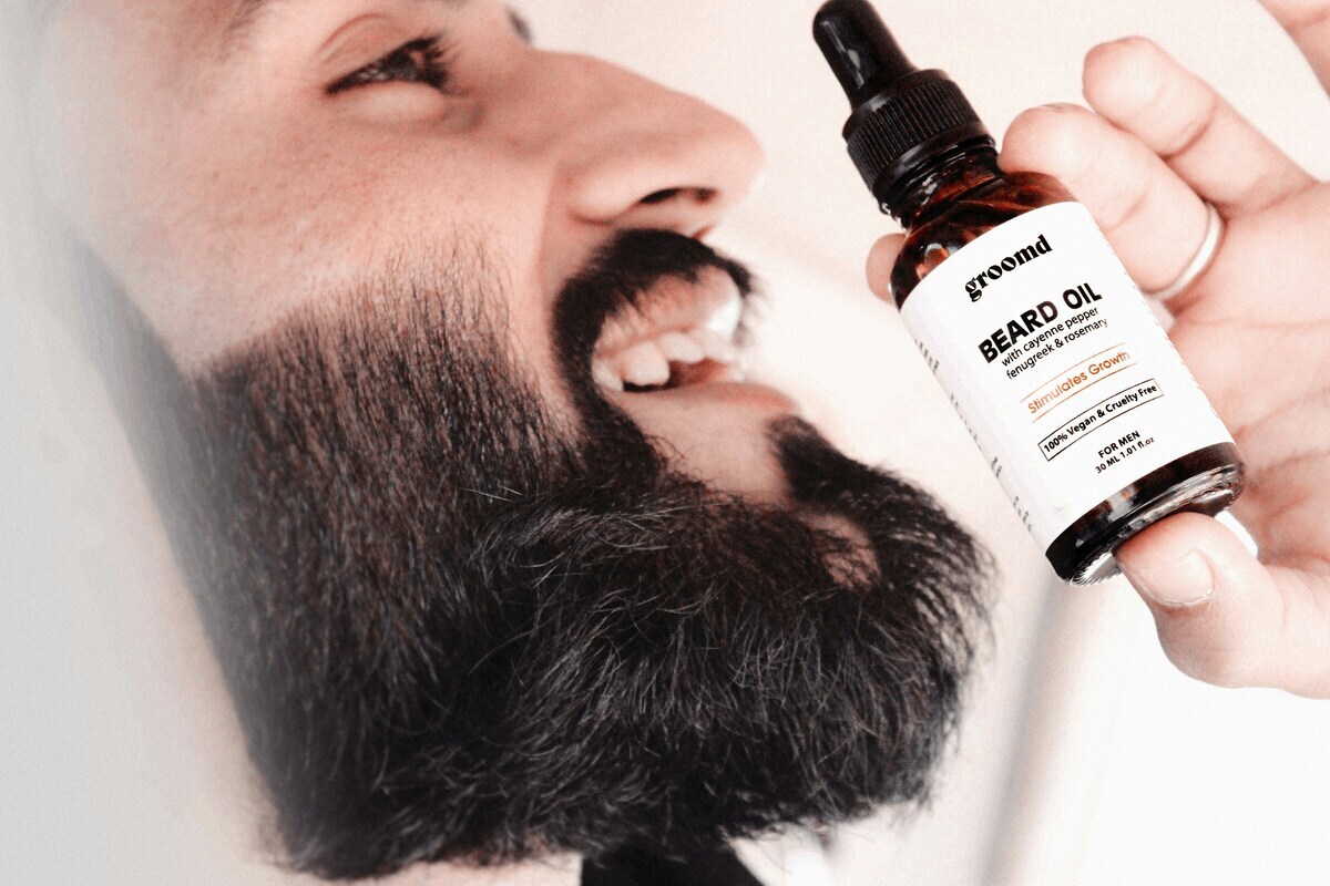 A man with a beard smiling while holding beard growth serum