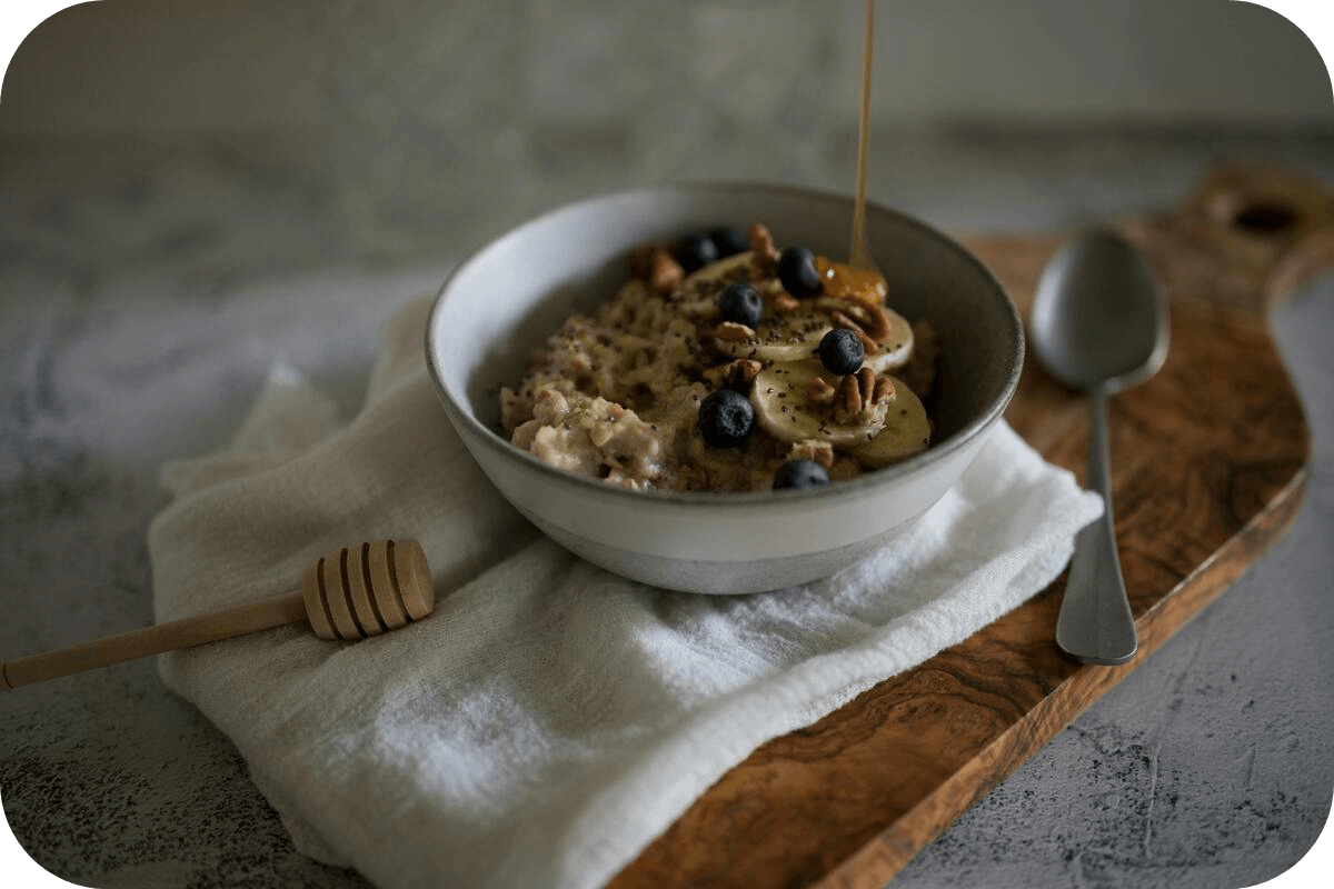 A bowl of porridge with banana, blueberries, nuts, and honey on a wooden board