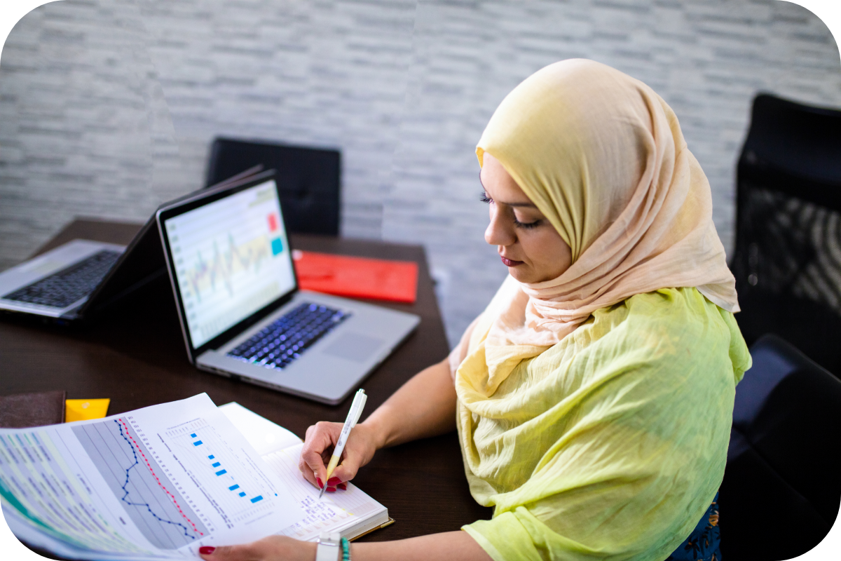 a women in hijab checking business files sitting in front of laptop